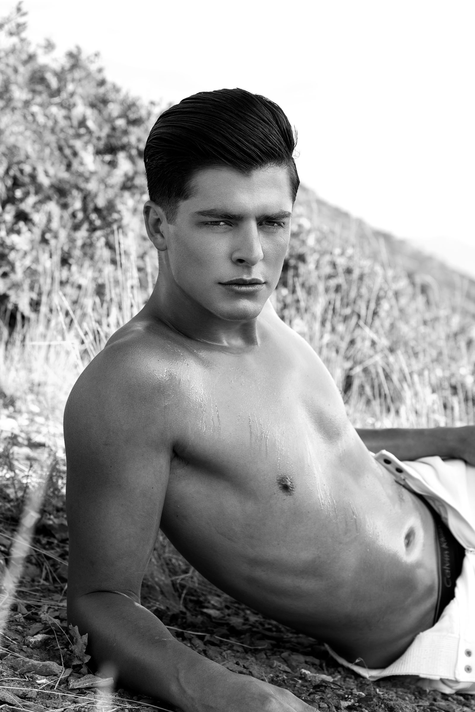Monochrome (black and white) editorial portrait of a shirtless male model in an outdoor location by Christopher Loke.